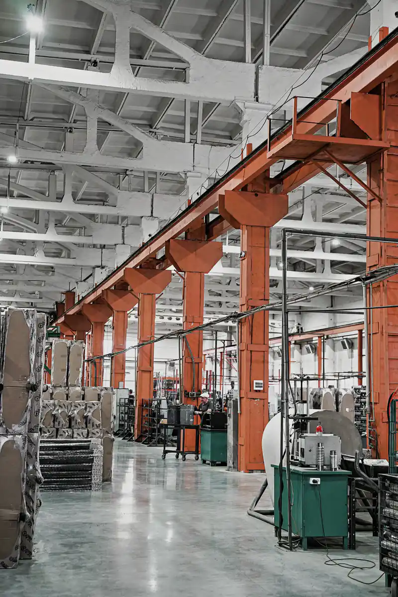 A production hall in black and white, with orange steel columns, a crane rail and packed goods along the aisle